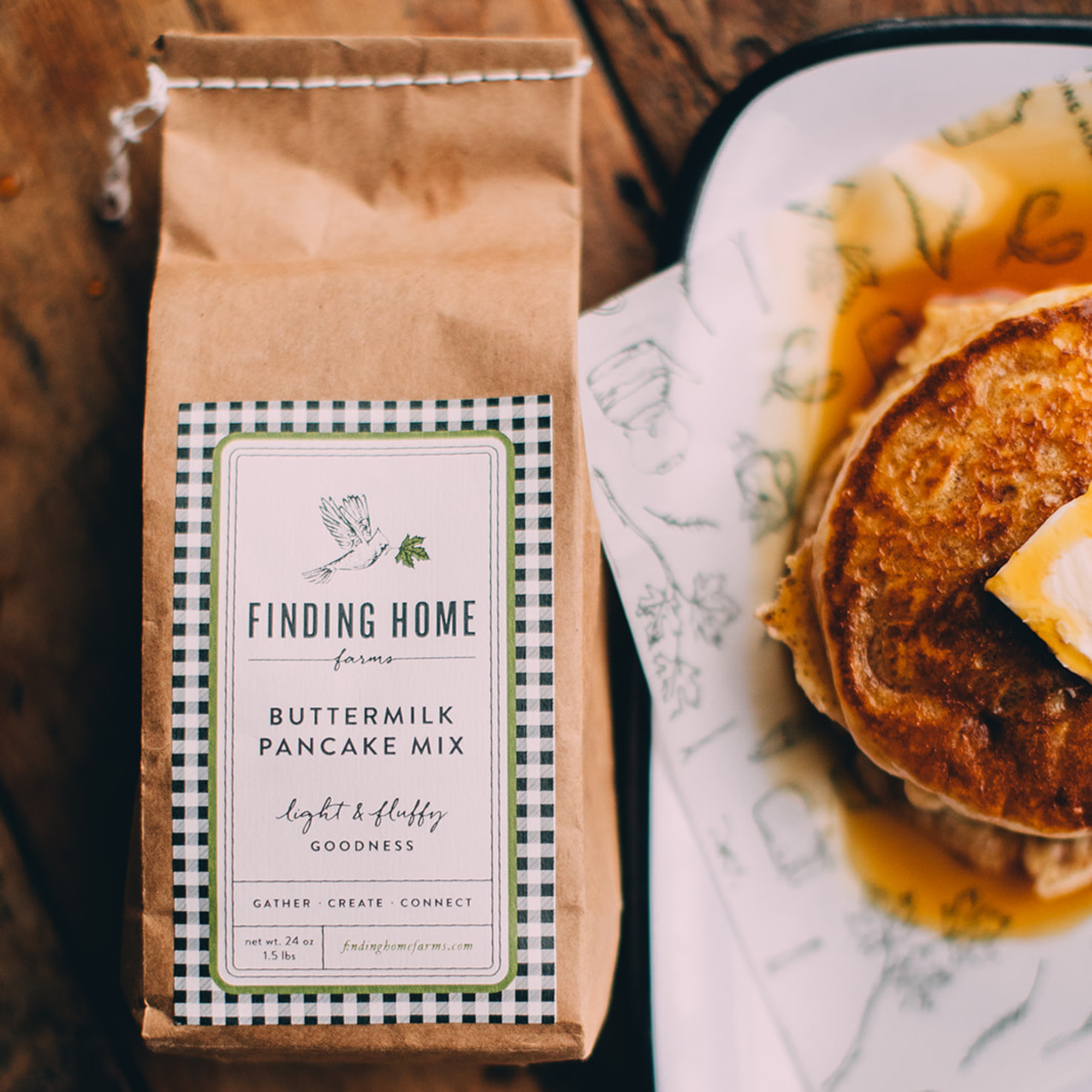 Blyskt Bag of Finding Home Farms Buttermilk Pancake Mix next to a plate of pancakes with syrup and butter.