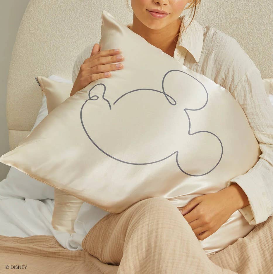 Blyskt Person holding a pillow with a Mickey Mouse design, sitting on a bed.