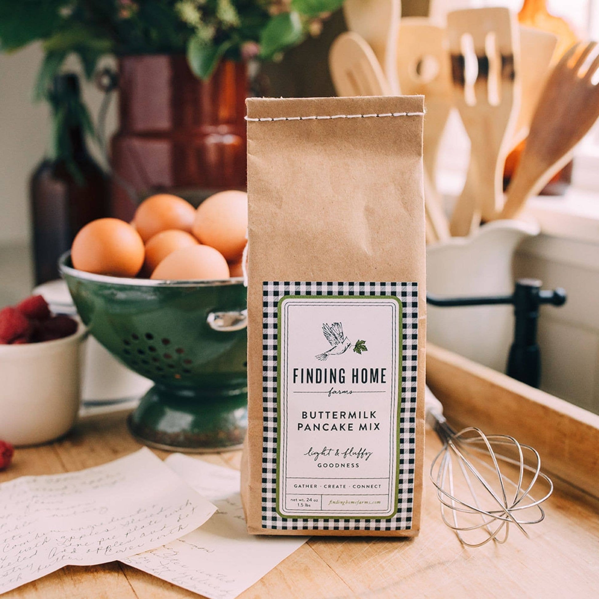 Blyskt Bag of Finding Home Farms Buttermilk Pancake Mix on a kitchen counter with eggs and utensils in the background.