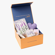 Gift box with lavender-themed items including cards and a heart-shaped pillow on a white background.