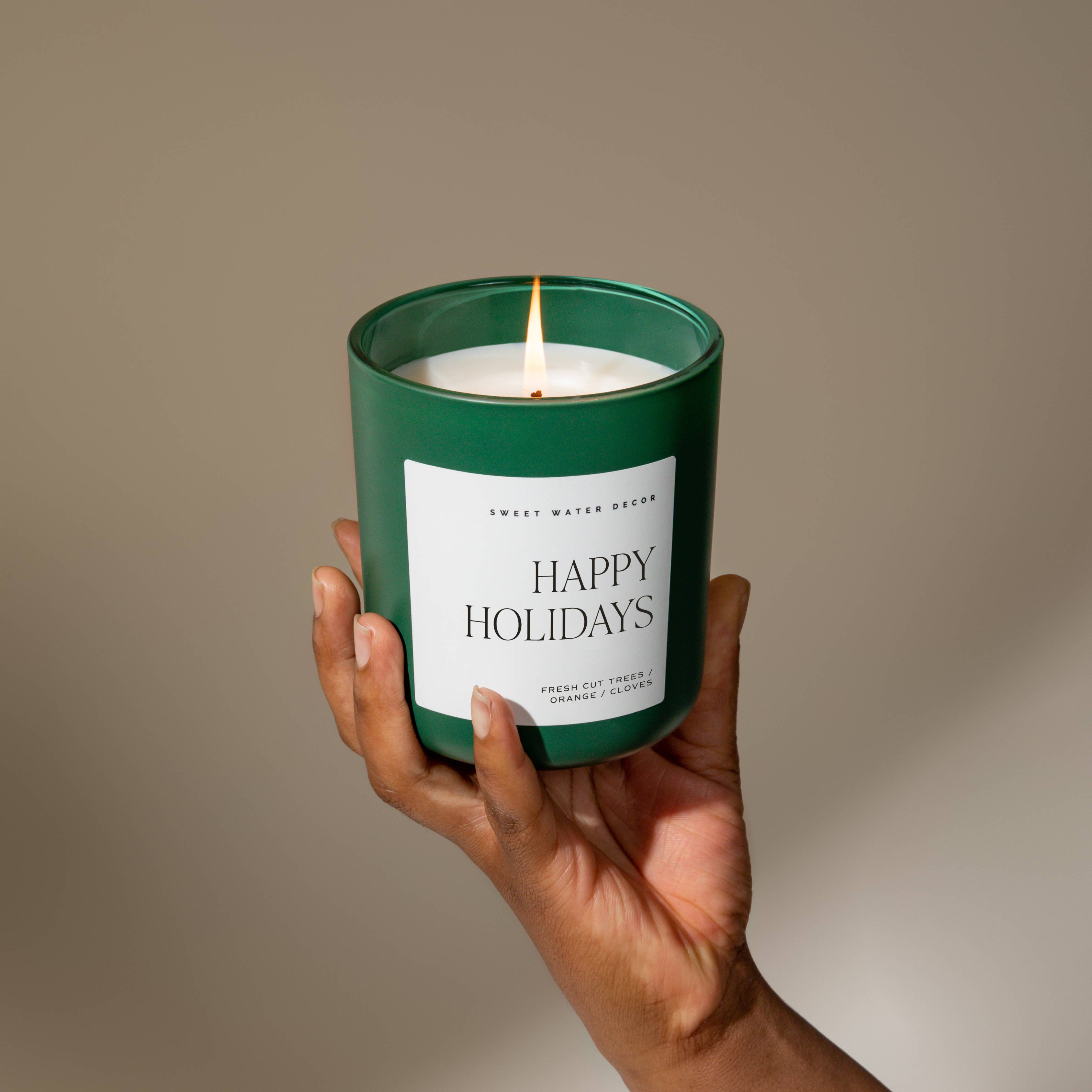 Blyskt Hand holding a 'Happy Holidays' candle with a green lid against a neutral background