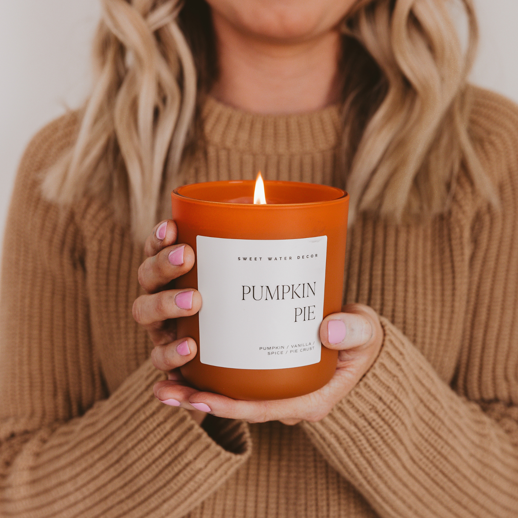 Person holding a 'Pumpkin Pie' candle in an orange container