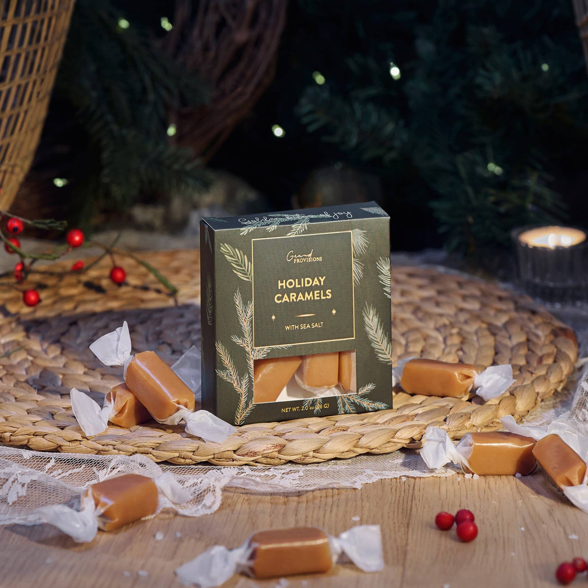Blyskt Box of Holiday Caramels with sea salt on a woven mat with a Christmas tree in the background