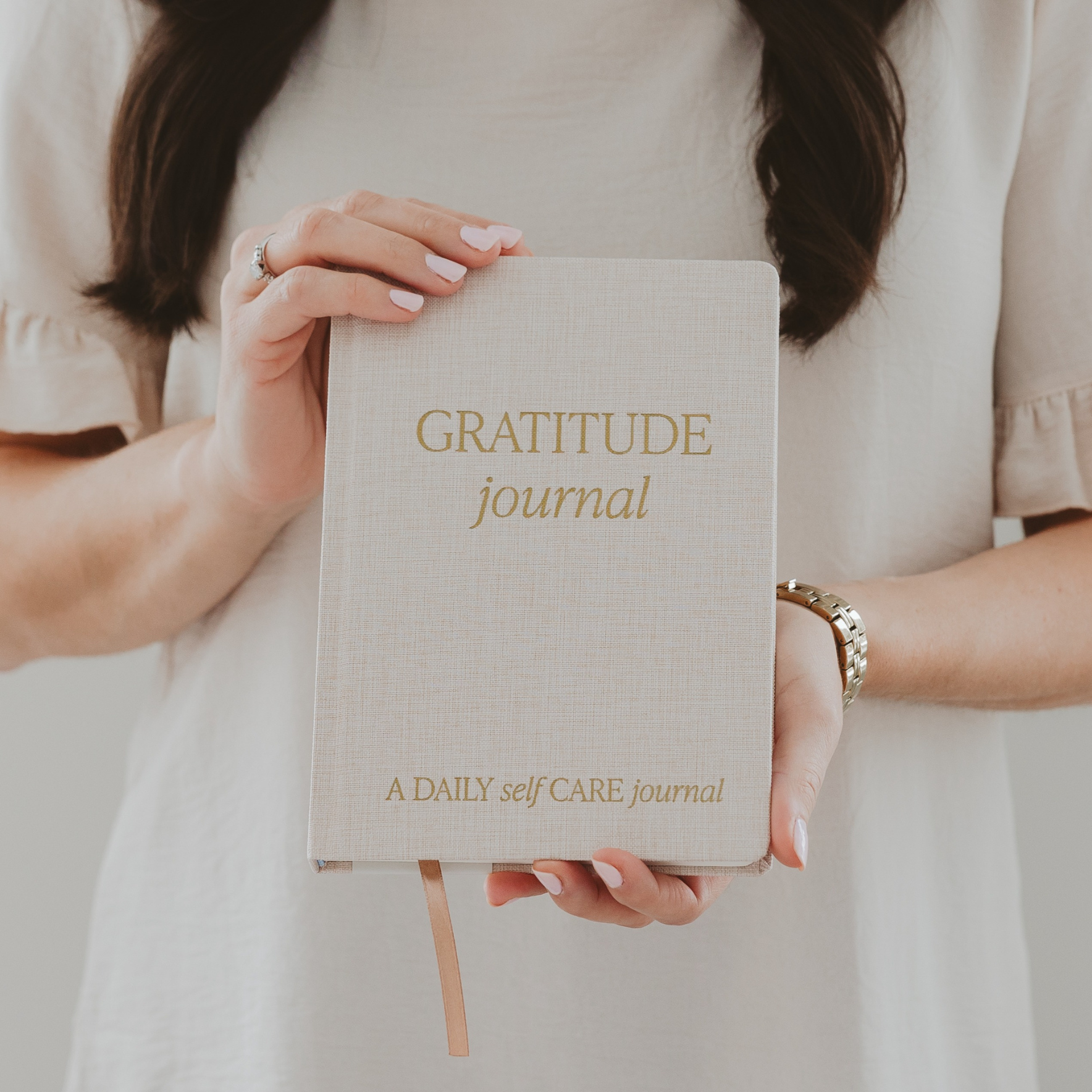 Blyskt Person holding a 'Gratitude Journal' with gold text on a plain background