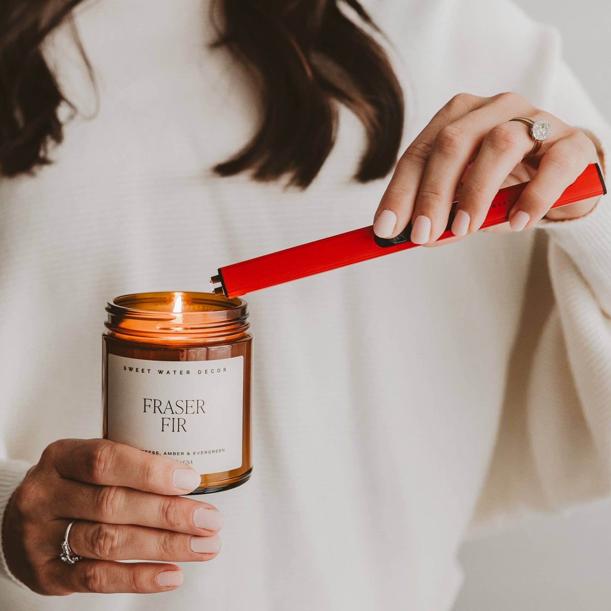 Blyskt Person lighting a Fraser Fir candle with a red lighter, wearing a white sweater.